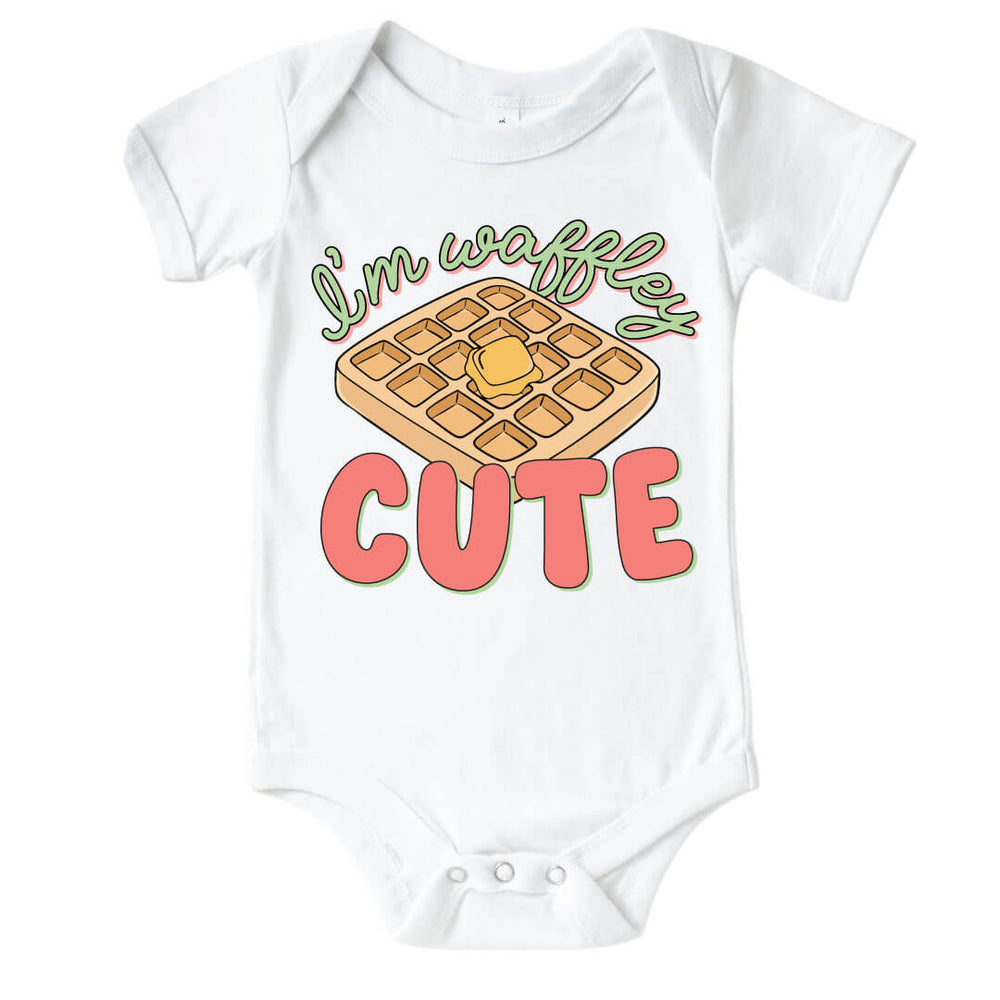 White "I'm Waffley Cute" Pink Graphic Bodysuit. Green and pink color font with waffle with butter in the center.  