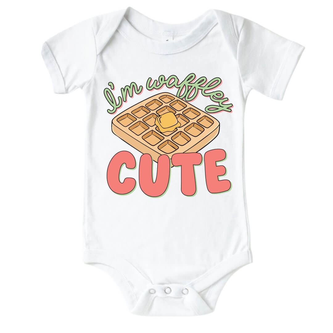 White "I'm Waffley Cute" Pink Graphic Bodysuit. Green and pink color font with waffle with butter in the center.  