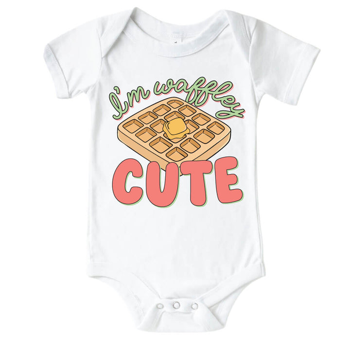 White "I'm Waffley Cute" Pink Graphic Bodysuit. Green and pink color font with waffle with butter in the center.  