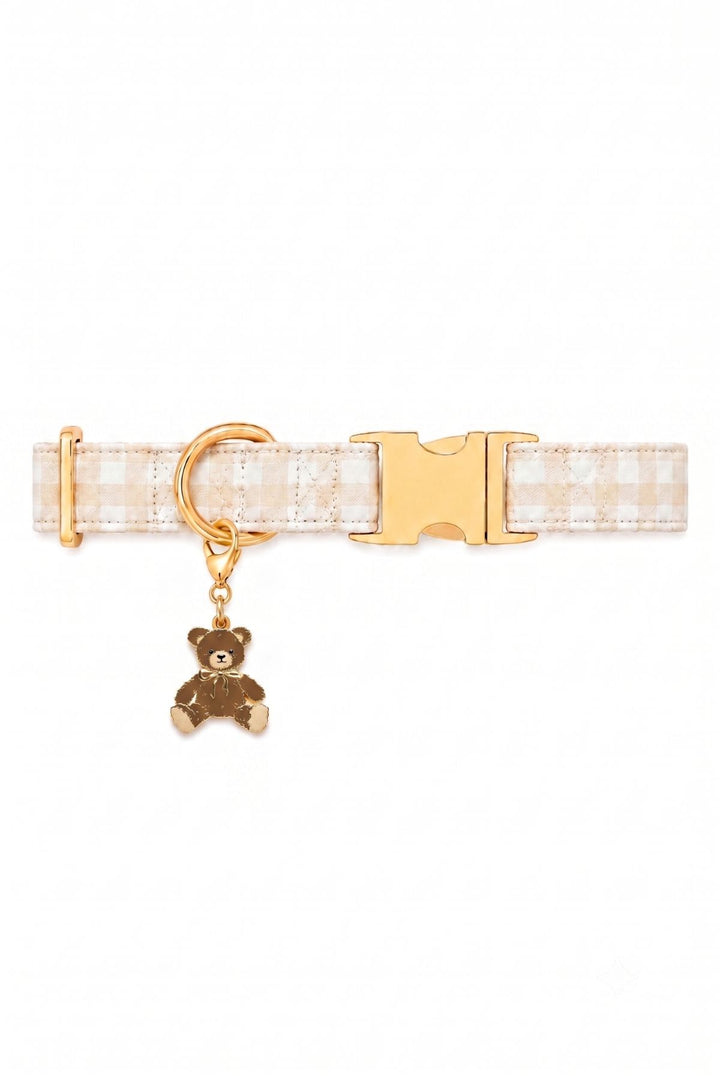 A Lane & Leash white and beige gingham check dog collar with gold-tone hardware, featuring a gold buckle, a gold ring, and a small hanging teddy bear charm.