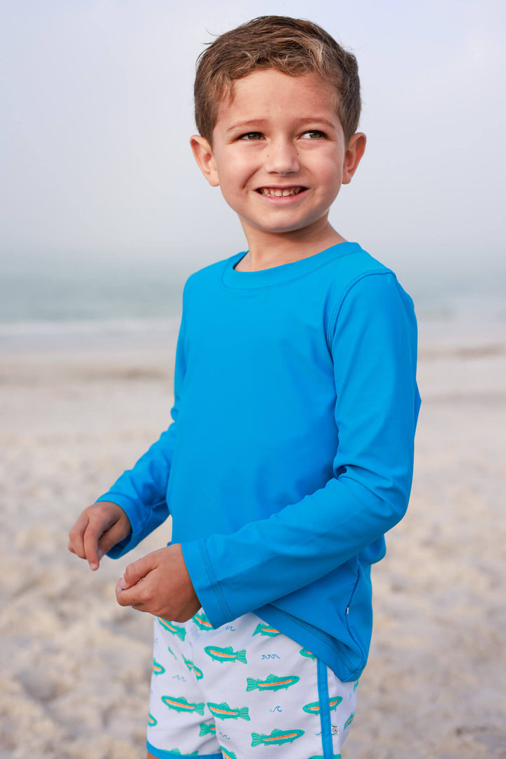 boy on beach in long sleeve rash guard shirt with trout swim trunks 