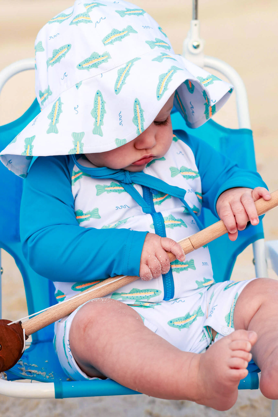 baby boy playing with fishing pole wearing tiny trout swim hat and romper 