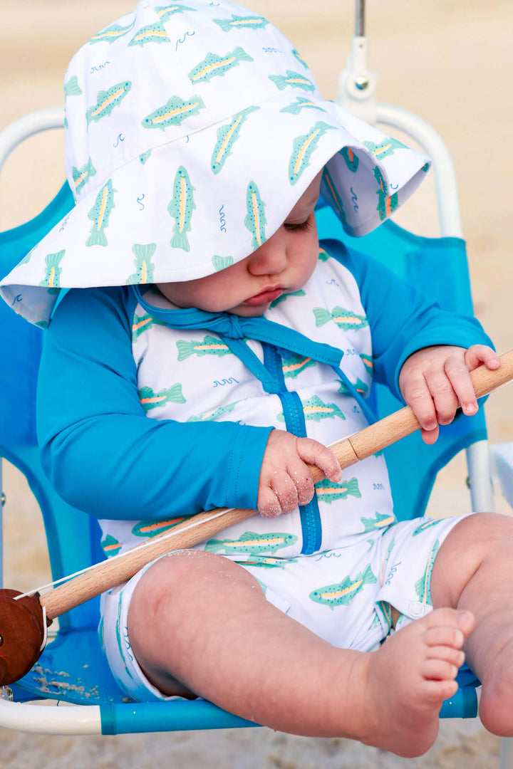 baby boy playing with fishing pole wearing tiny trout swim hat and romper 