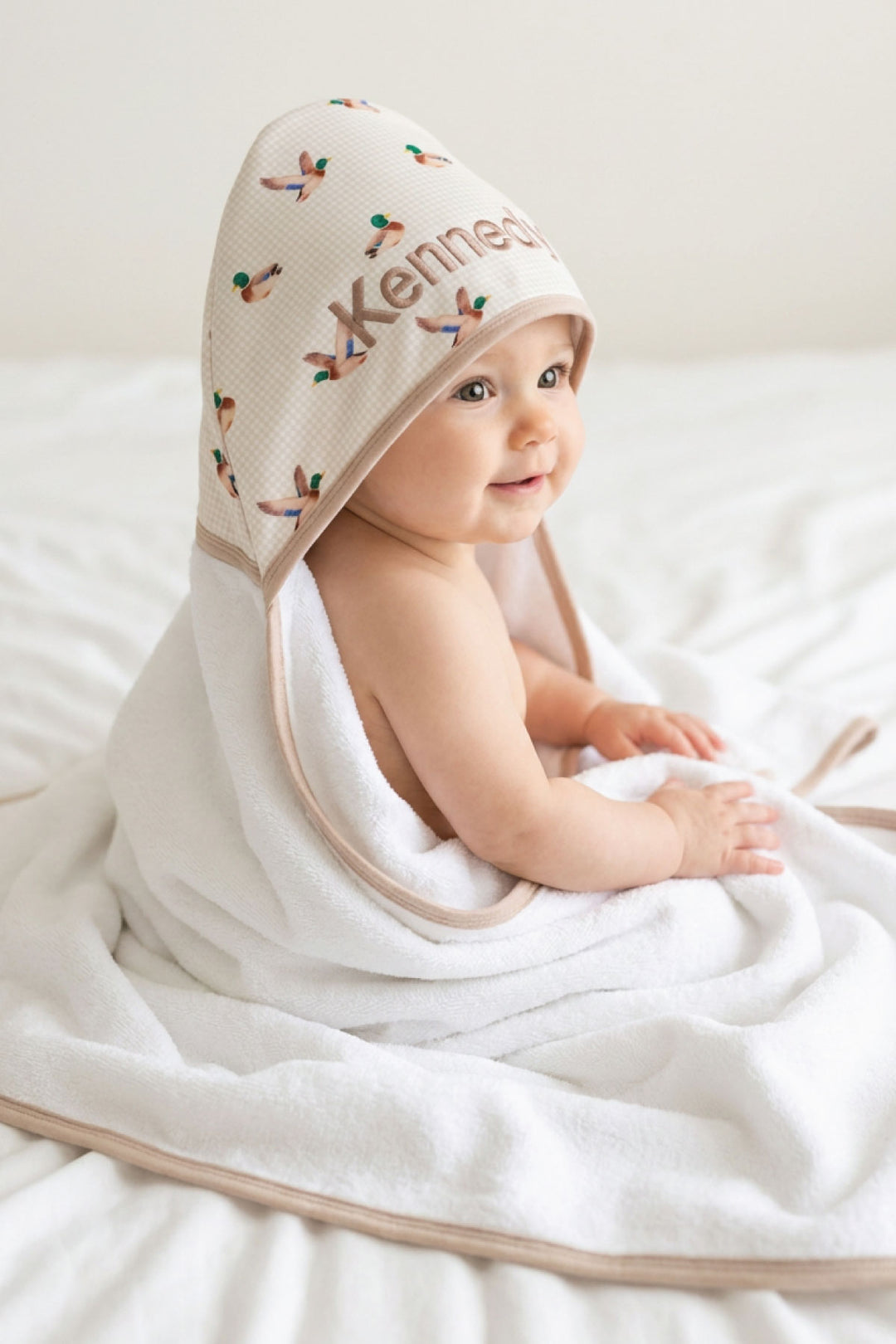 Smiling baby wearing a personalized little mallard duck print bamboo hooded towel with name embroidered on hood, side profile view
