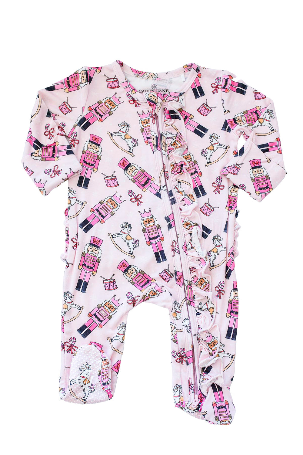 Flat lay of Caden Lane's pink toy soldier print ruffle zip-up pajamas, featuring nutcrackers and rocking horses.