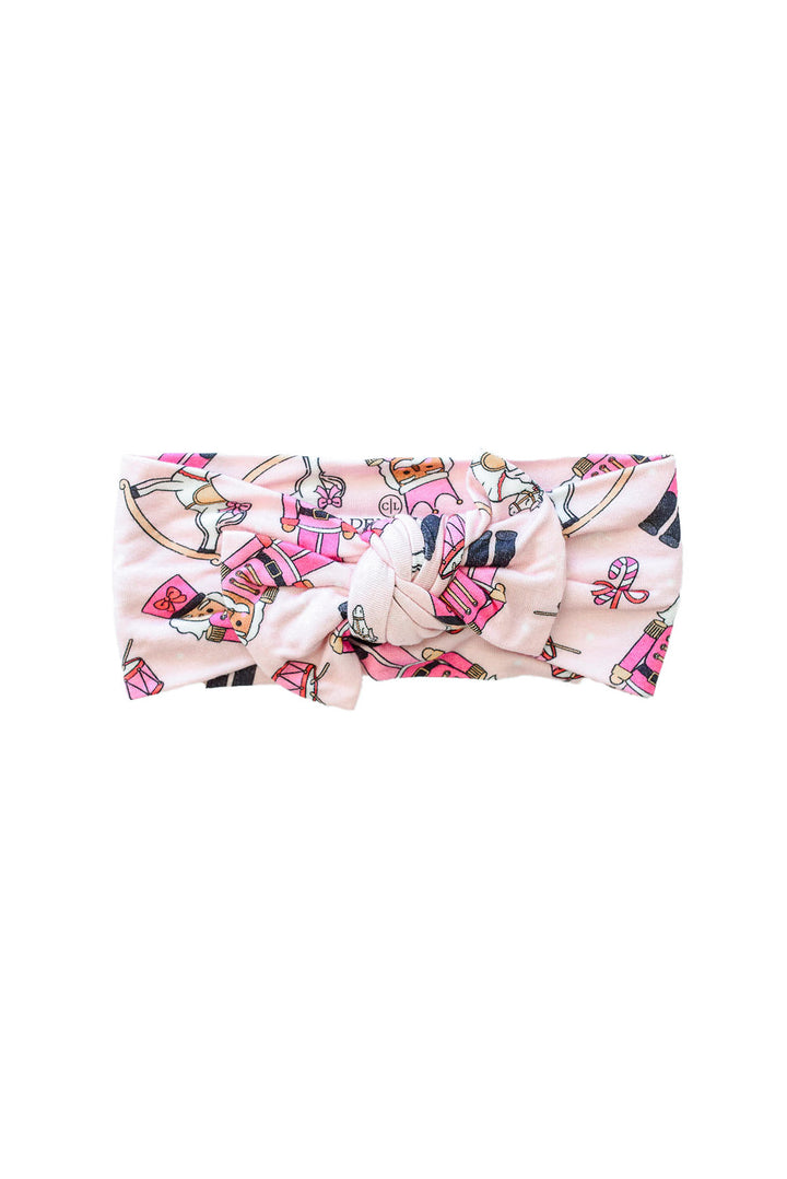 Flat lay of Caden Lane's pink toy soldier print knot headband, featuring nutcrackers and rocking horses.