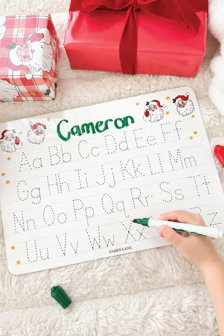 Caden Lane personalized Christmas handwriting practice board featuring the name "Cameron" in festive red and green plaid lettering with traceable uppercase and lowercase alphabet, creating a fun personalized holiday learning gift for kids.