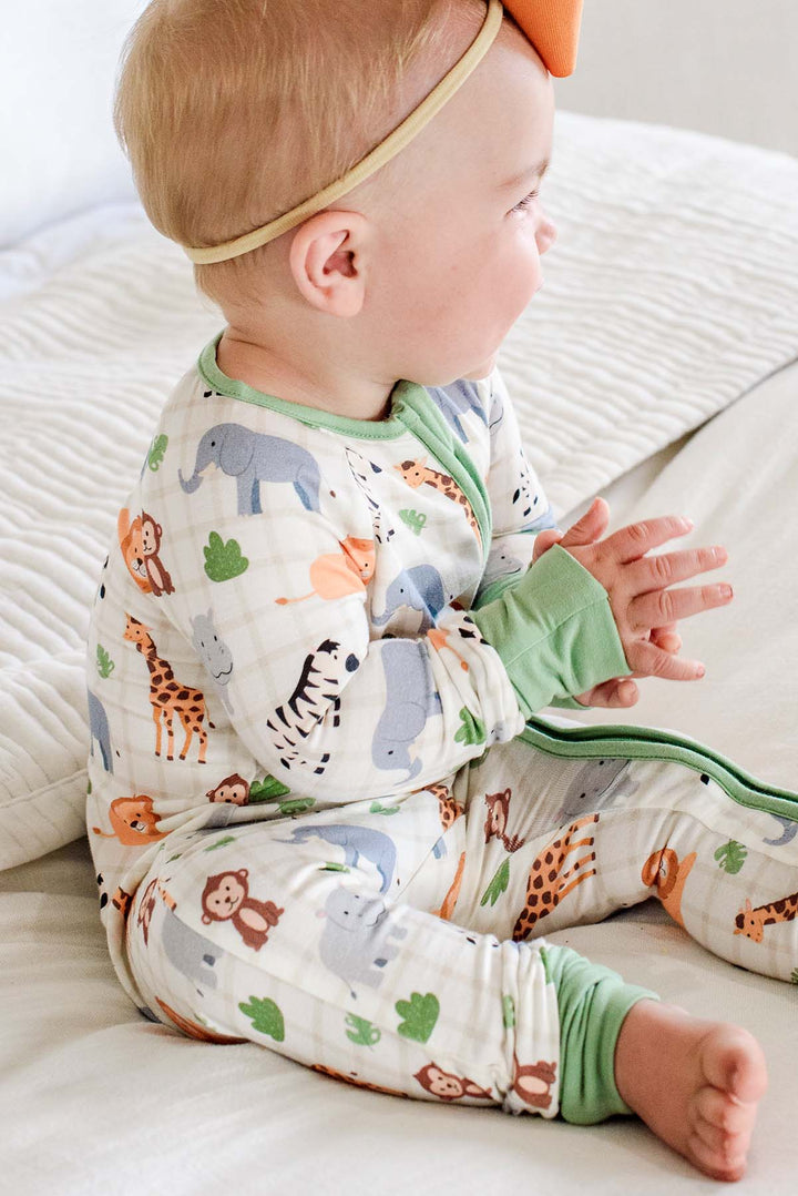 Side view of a baby girl clapping her hands while sitting in a Caden Lane Wild Child convertible zip romper with green cuffs, paired with an orange bow headband.