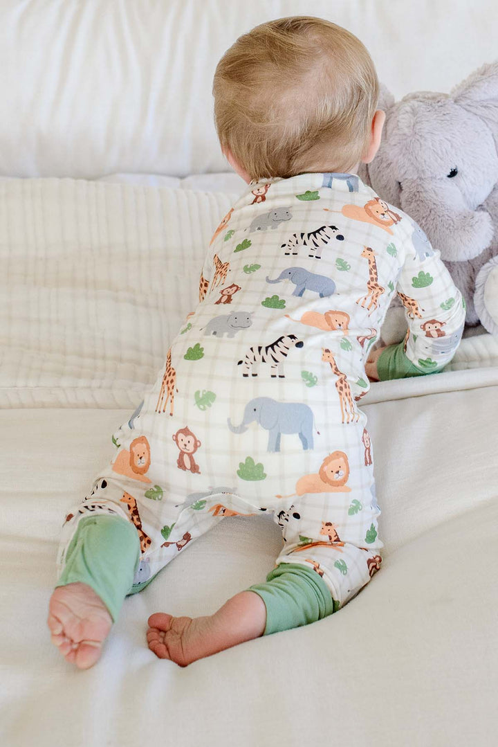 Back view of a baby boy crawling toward an elephant plush in a Caden Lane convertible zip romper in a Wild Child print with green cuffs.