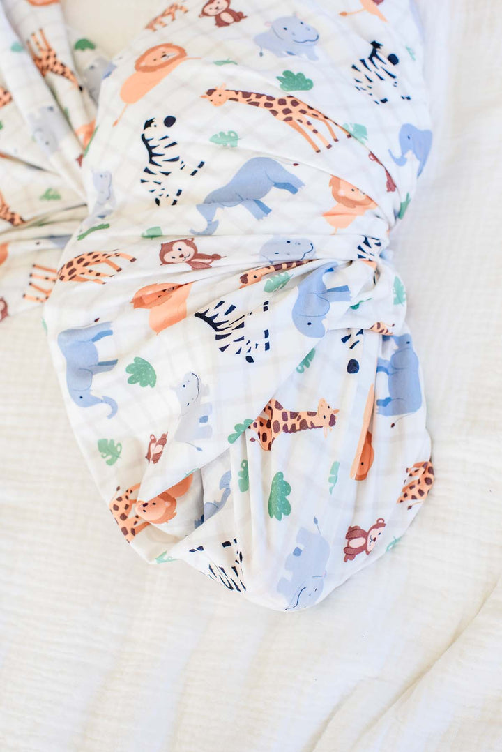 Close-up of the gathered bottom of a Caden Lane swaddle blanket in a Wild Child print featuring giraffes, elephants, zebras, lions and hippos on cream plaid.
