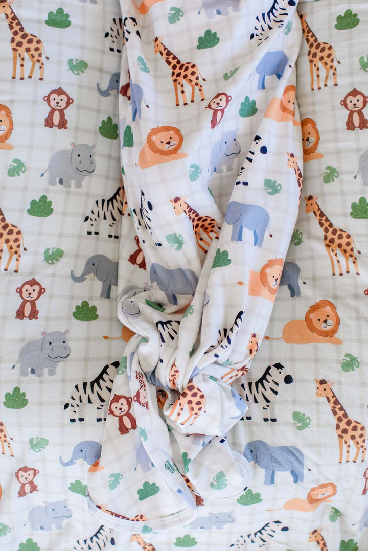 Close-up of the knotted bottom of a Caden Lane gown in a Wild Child print, resting on a matching blanket with giraffes, hippos, monkeys and zebras.