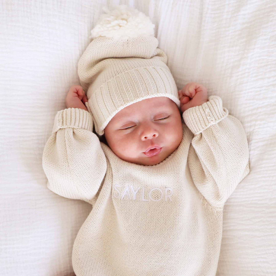 long sleeve beige personalized sweater romper for babies embroidered with name with matching pom pom beanie 