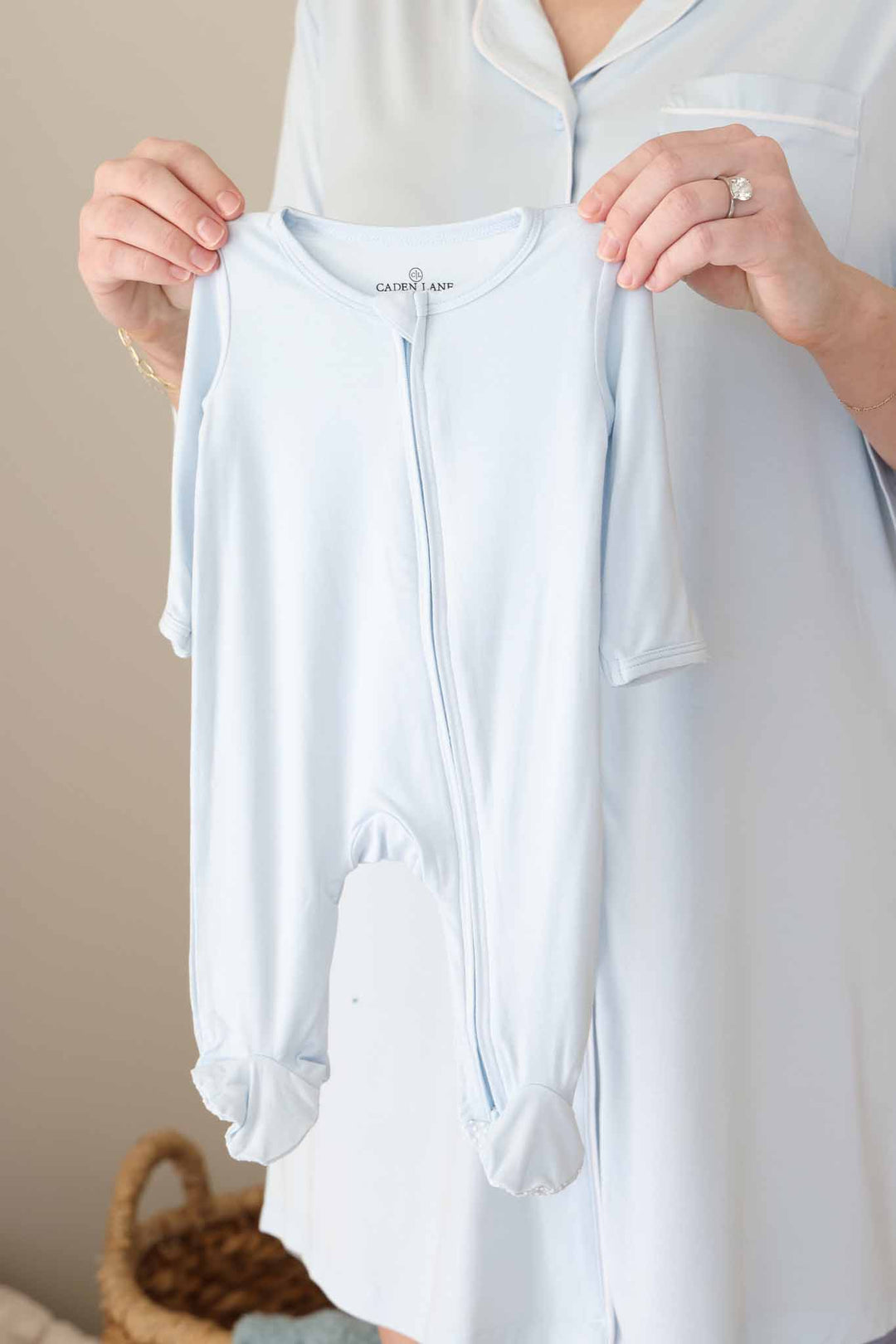 mom holding up a light blue baby zipper footie 