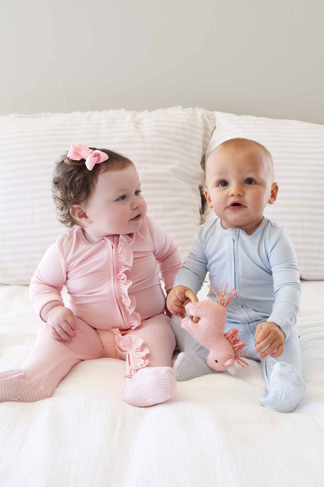 two babies sitting next to each other in pastel footies blue and pink 