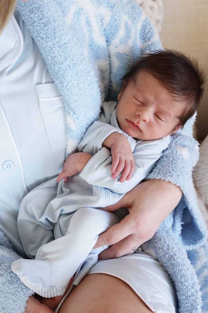 baby boy laying in mom's arms in light blue zipper footie while she wears a matching gown with a plush robe on top 