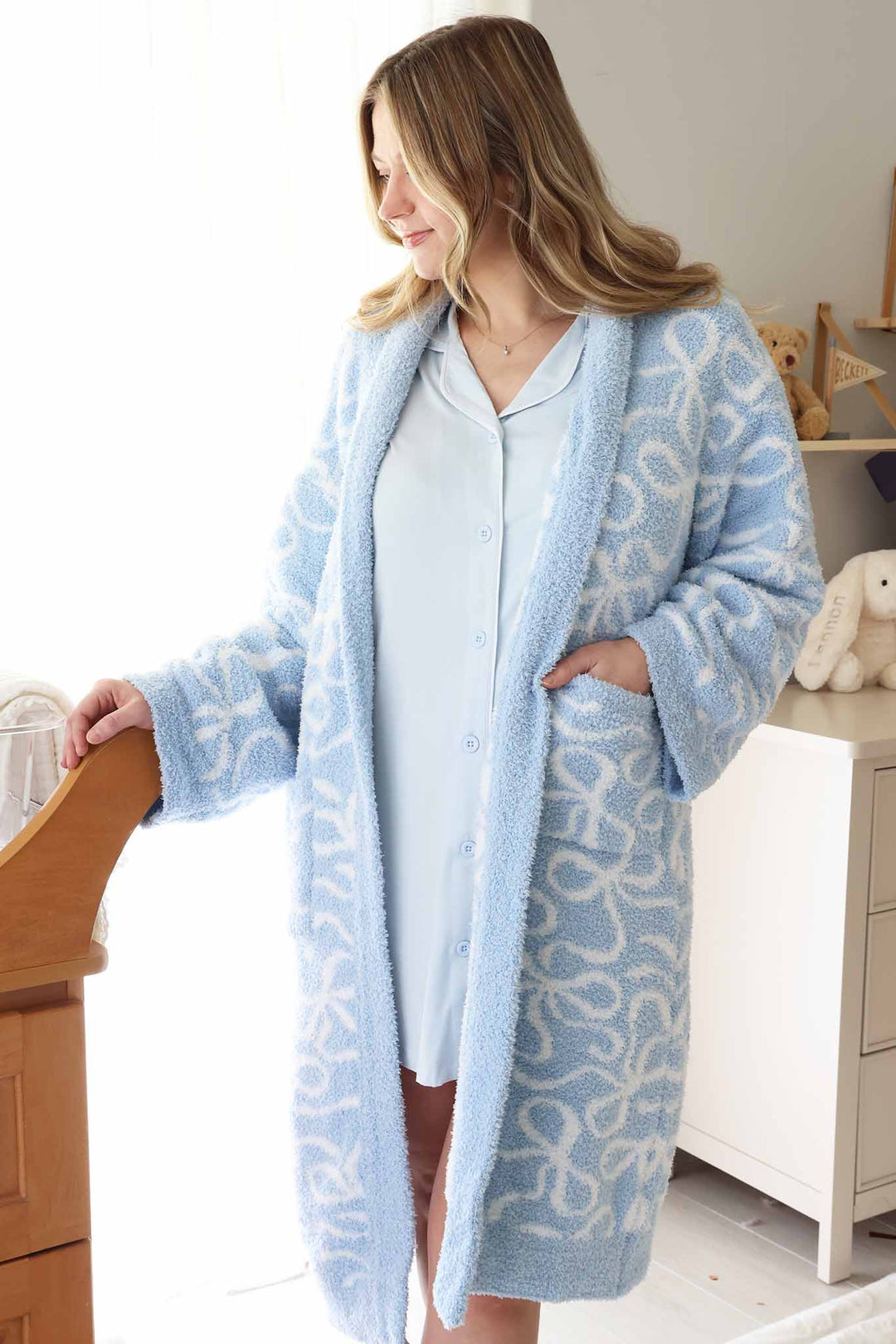 mom standing next to bassinet in baby blue labor & delivery gown with a plush blue and white bow robe 