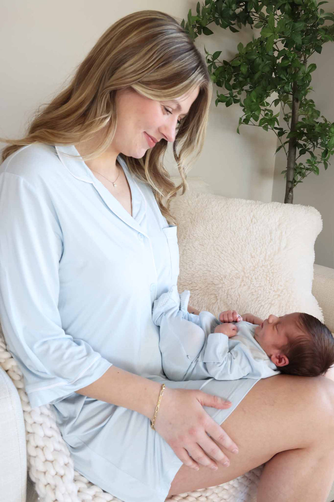 mom wearing light blue labor & delivery gown with a baby sitting on her lap in matching footie pajama 