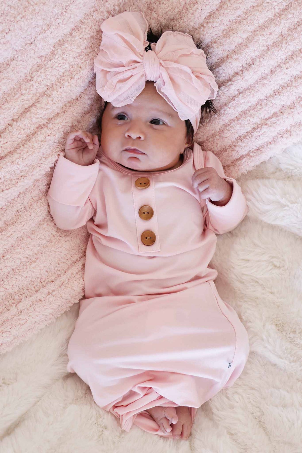 baby girl laying on white and pink blankets in baby pink newborn knot gown with a matching pink ruffle bow 