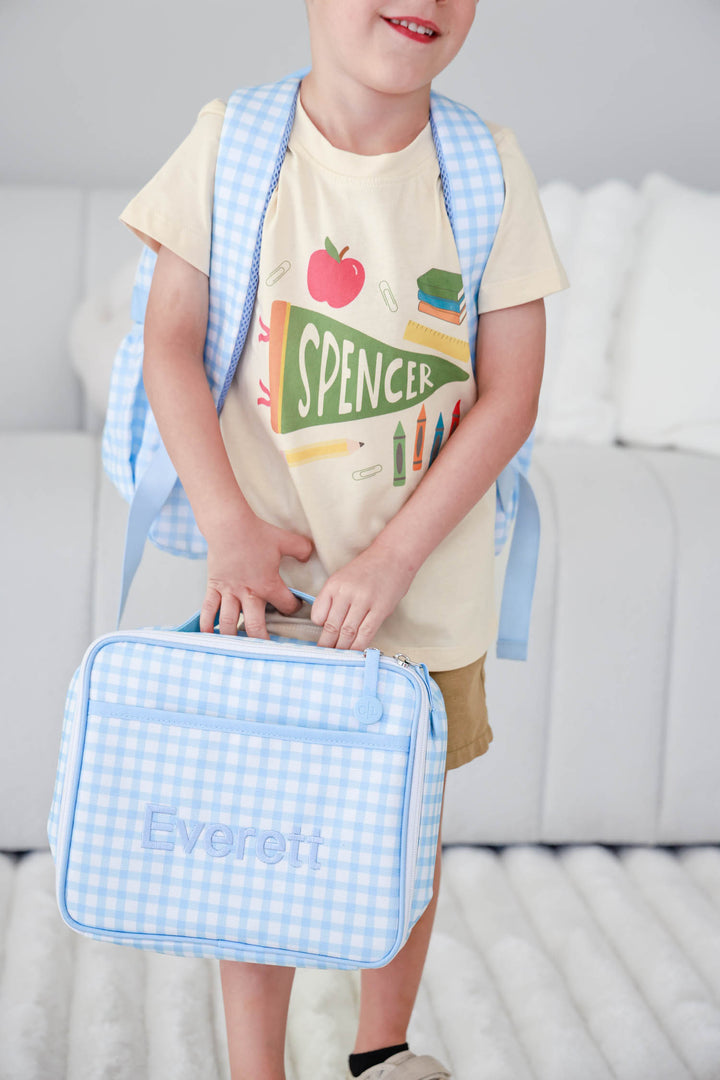 boy wearing personalized back to school tee holding a blue gingham embroidered lunchbox and wearing matching backpack