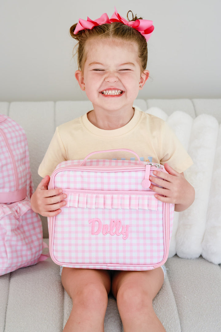 smiling girl holding pink gingham embroidered lunchbox