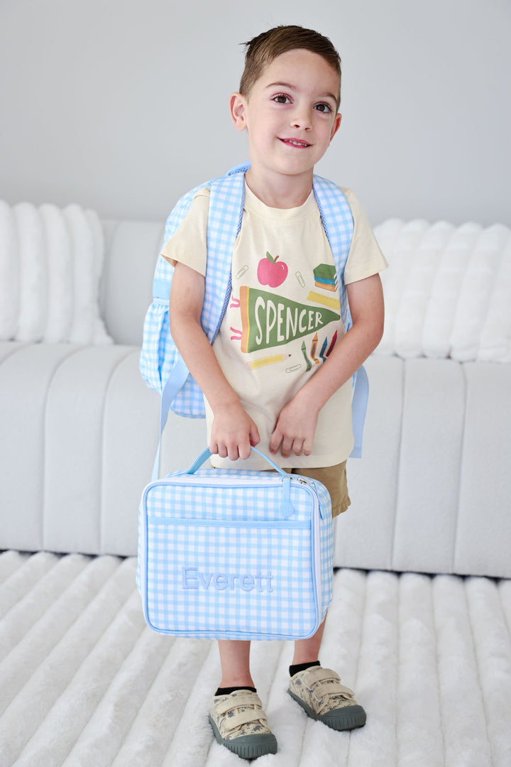 boy holding matching blue gingham embroidered backpack and lunchbox