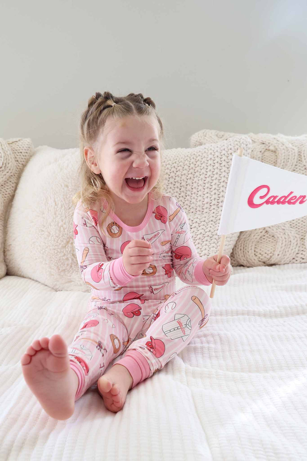 girl sitting on bed in ballpark babes long sleeve pajama set with embroidered flag banner 