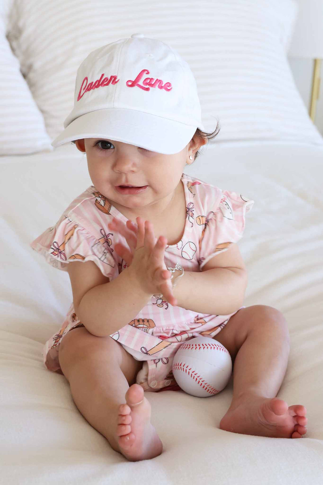 baby girl sitting in ballpark baby ruffle skirt bodysuit wearing a white embroidered hat 