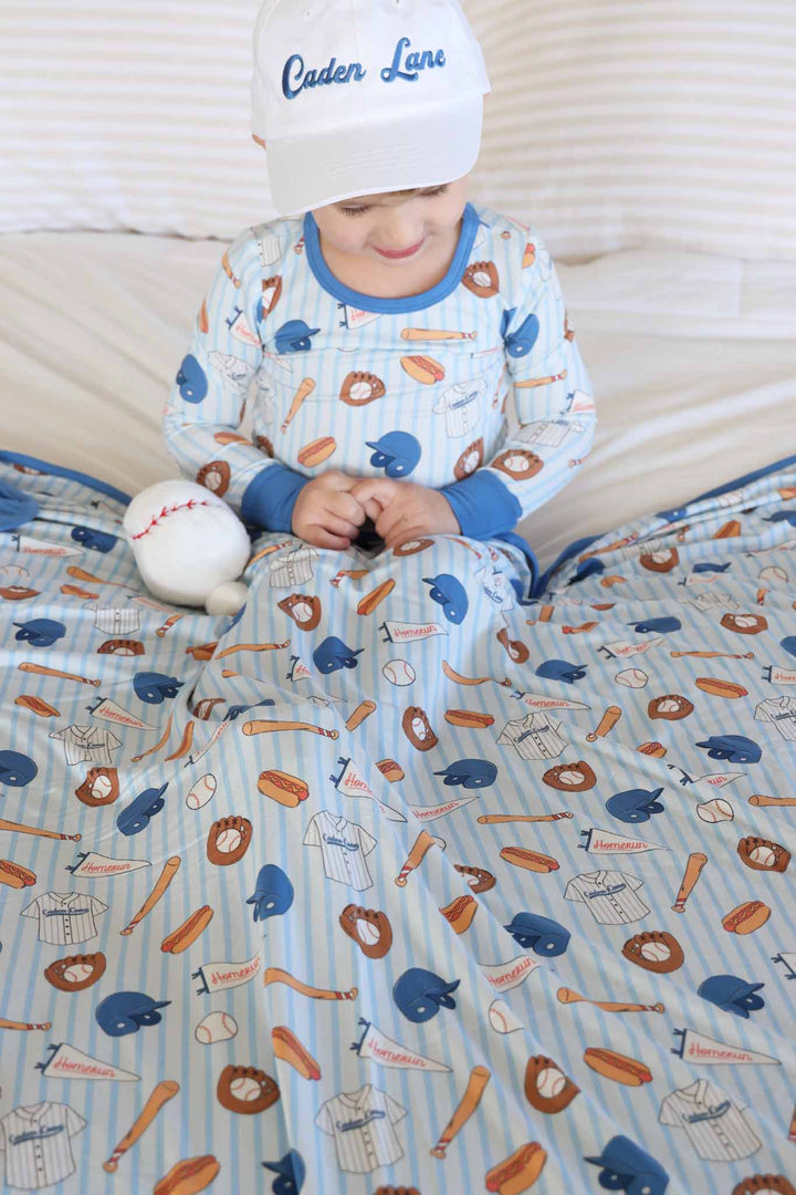 boy wearing baseball themed two piece pajama set with a matching bamboo blanket across his lap 