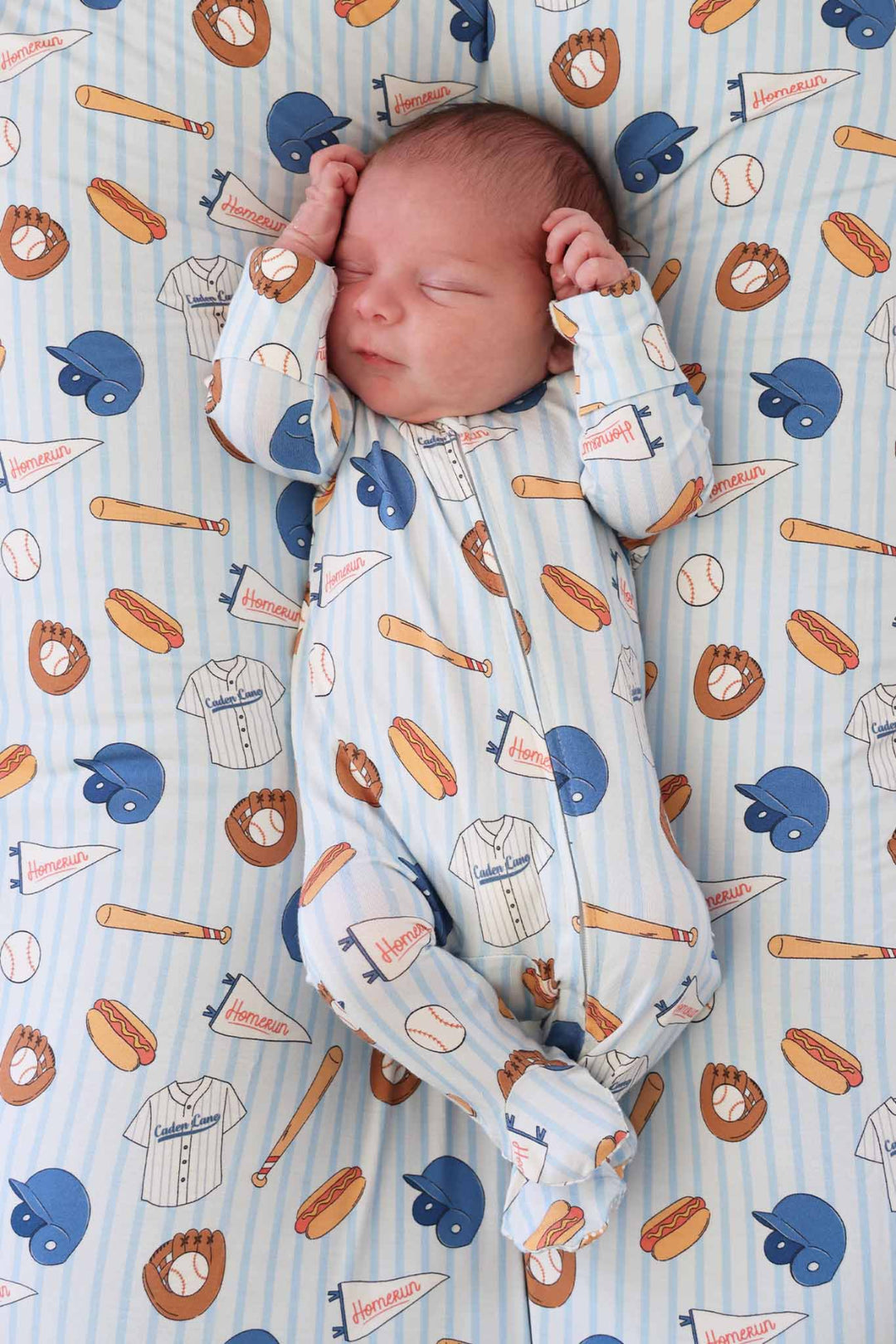 Newborn baby sleeping in a onesie with sports-themed pattern on a matching blanket