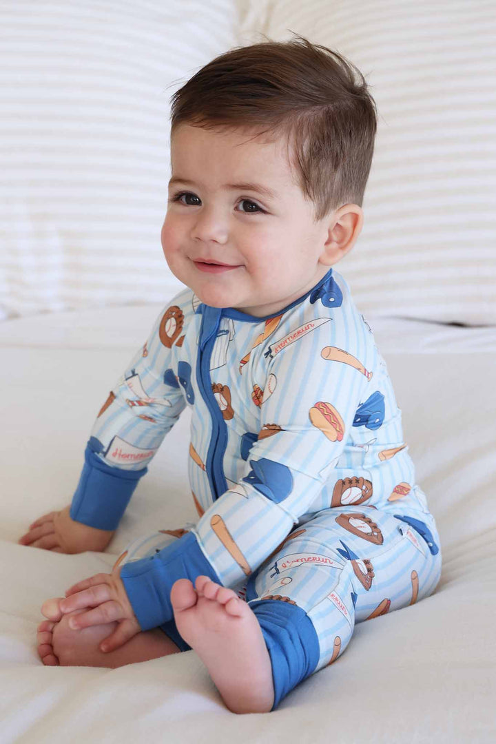 boy sitting on bed in baseball themed bamboo convertible zip romper 