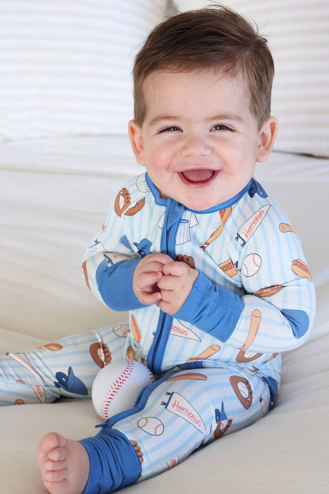 smiling baby boy in blue striped bamboo convertible zip romper with baseball things