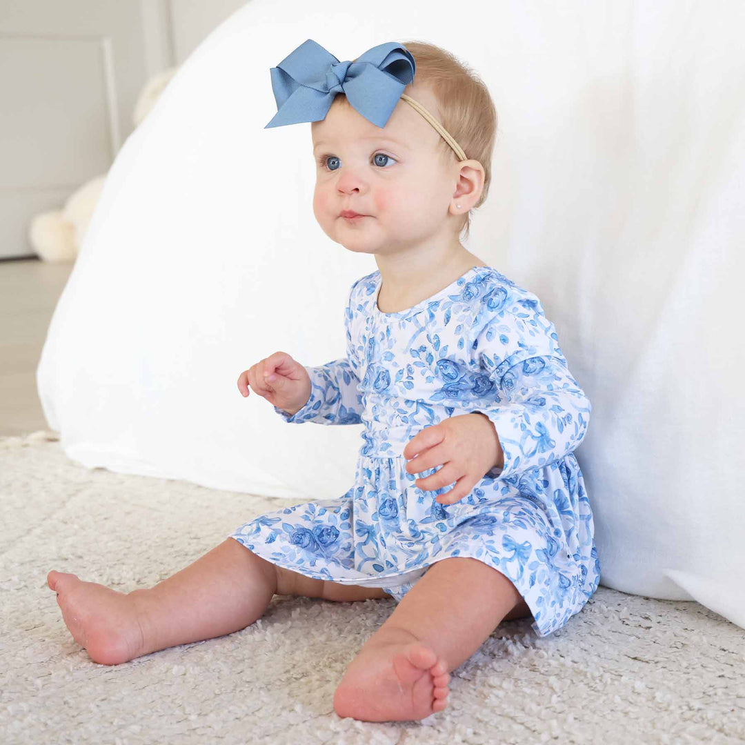 toddler girl sitting on floor in blue and white floral and bow long sleeve skirt bodysuit