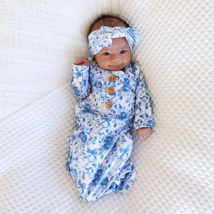 newborn baby girl wearing a blue and white floral and bow long sleeve knot gown with matching bow headwrap