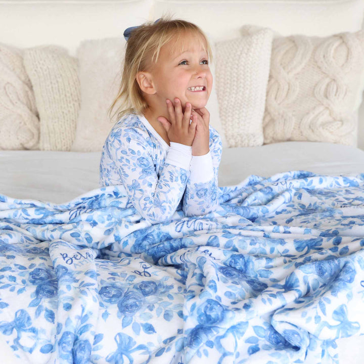 girl wearing blue and white floral pajama set covered with a matching personalized blanket 