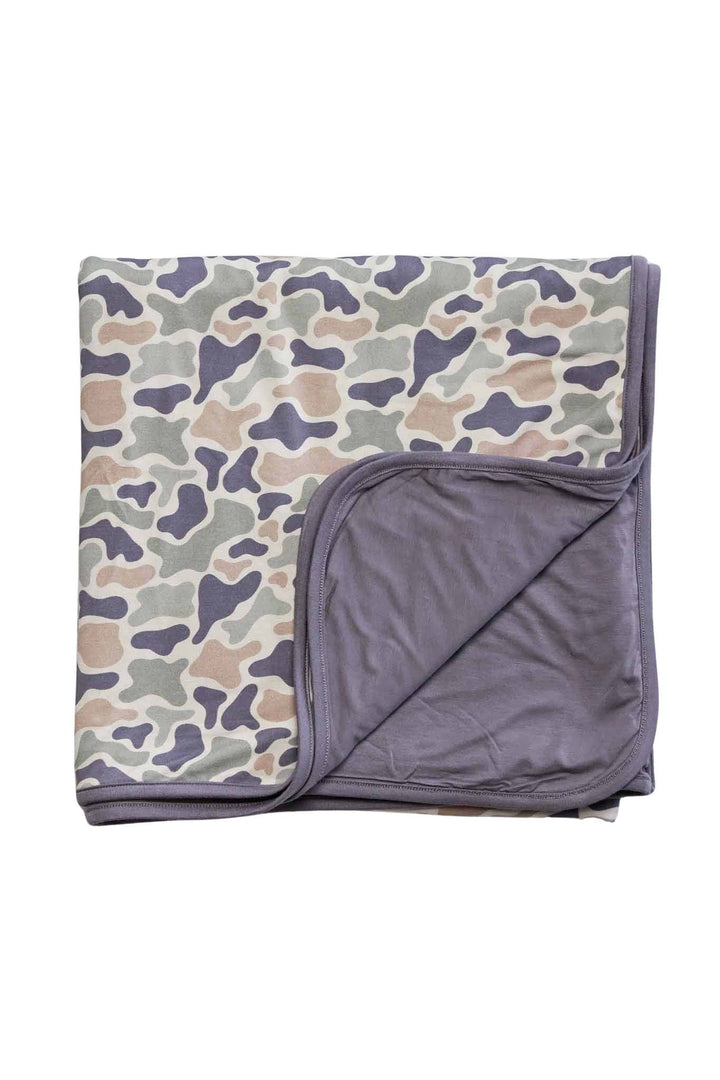 Double-sided bamboo blanket folded flat with corner turned back showing camo cutie print exterior and solid lavender gray interior