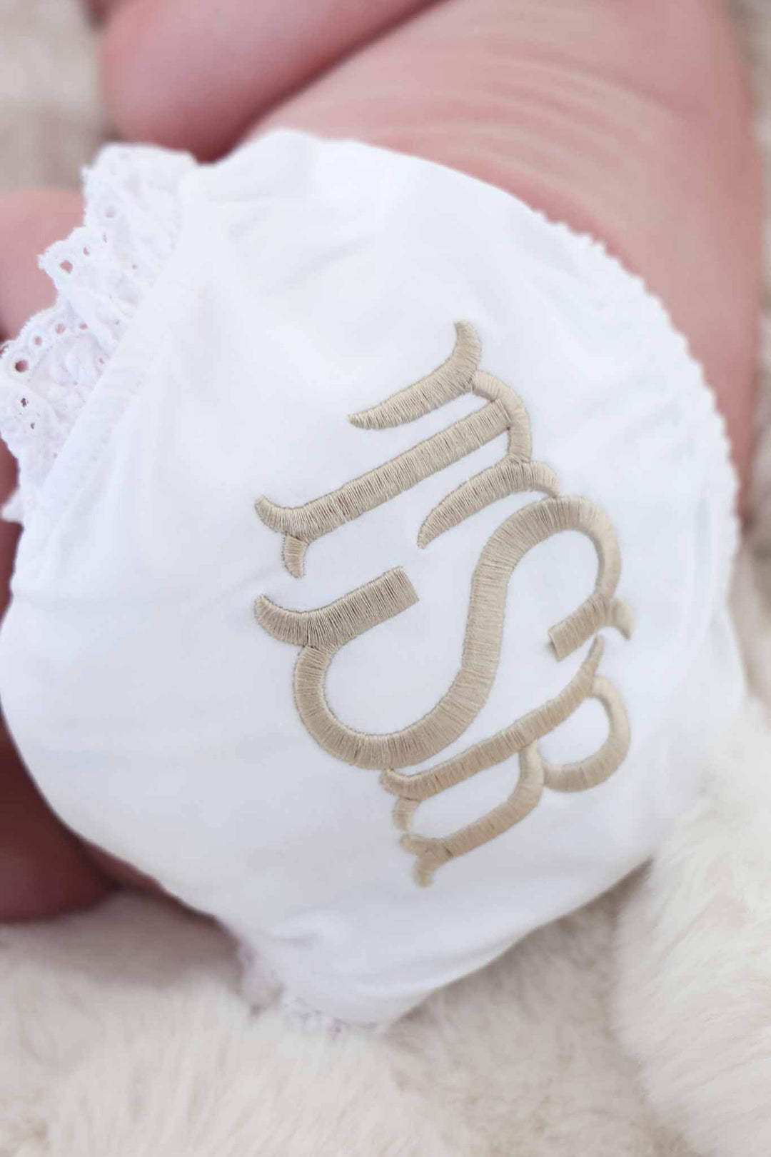 baby laying on its side in monogrammed bloomers with lace leggs and neutral thread 