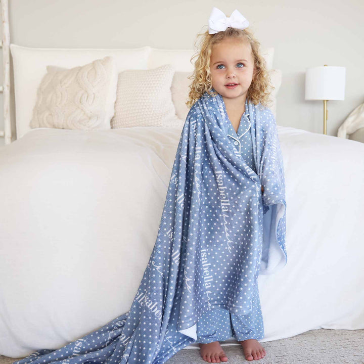 girl wearing a long sleeve button up lounge set flare pants in dusty blue with white polka dots with a matching personalized blanket wrapped around 