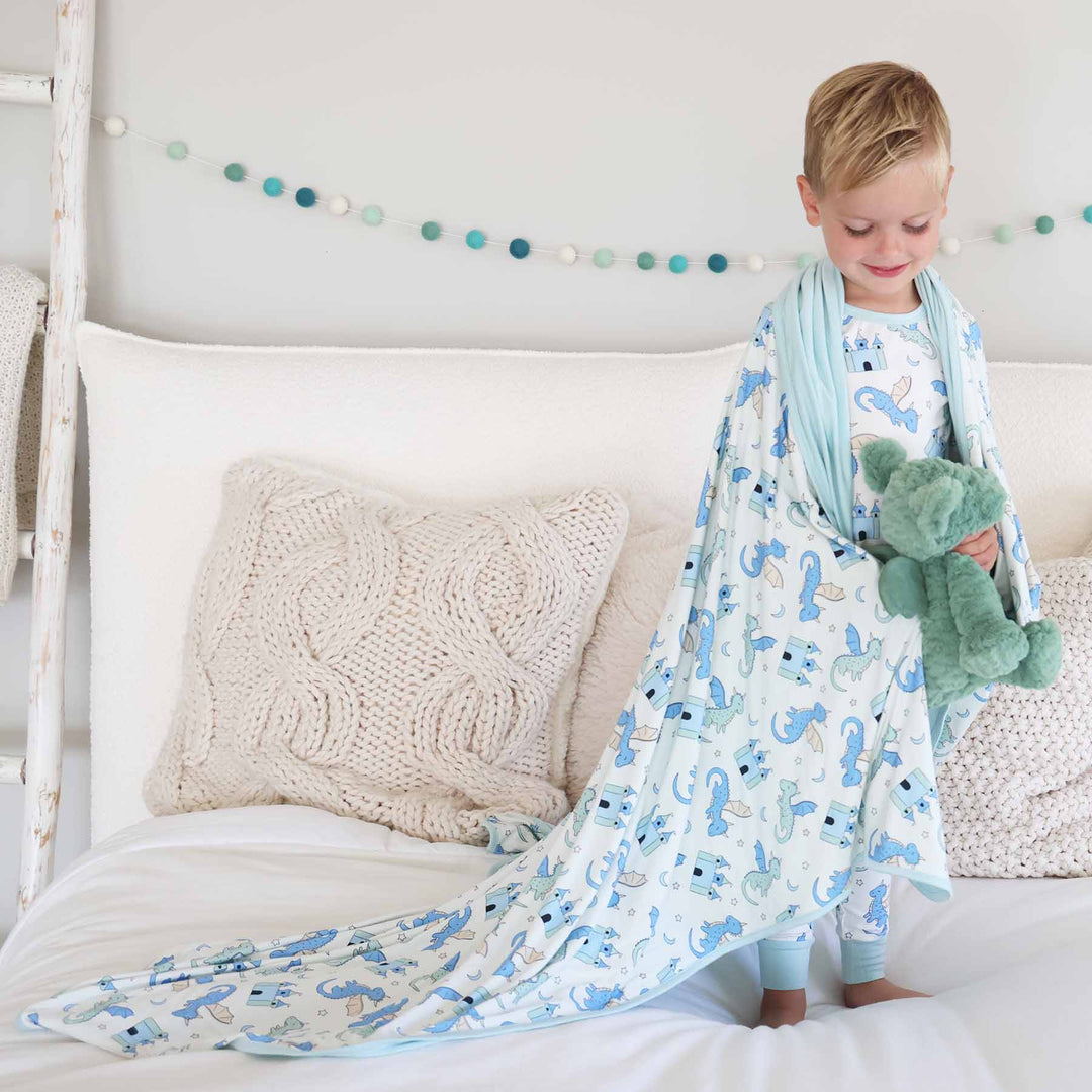 Boy standing barefoot on bed holding blanket decorated with castles and dragons