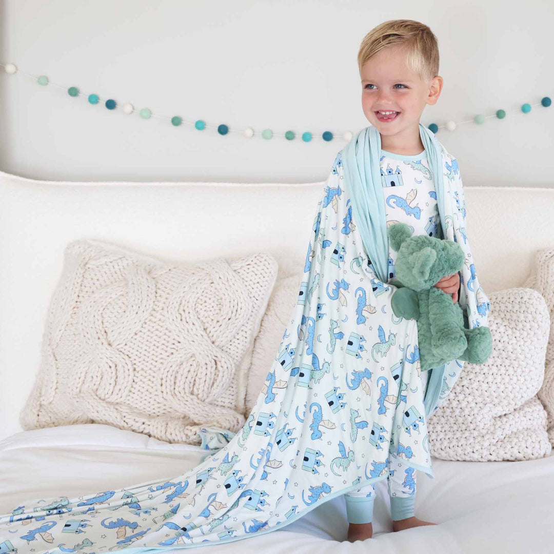 Boy smiling while holding green plush toy and dragon print blanket