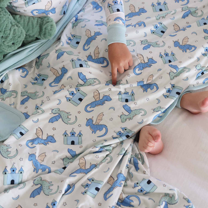 pointing child covered in fantasy print blanket featuring blue and green dragons