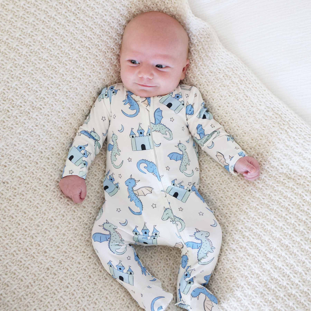 Baby wearing cream footie pajamas with blue and green dragon and castle print
