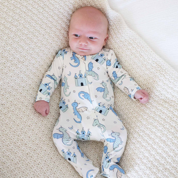 Baby wearing cream footie pajamas with blue and green dragon and castle print