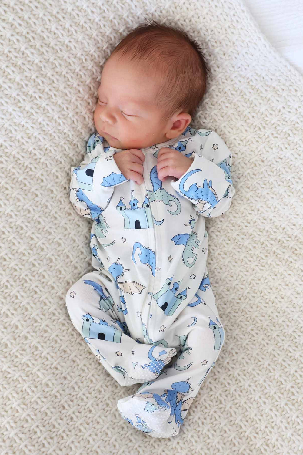 Infant lying on a knit blanket in dragon-themed zipper footie
