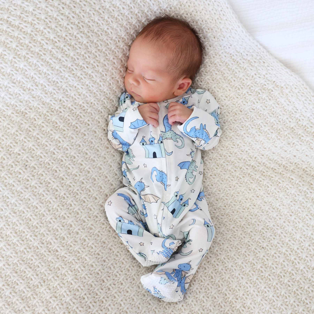 Infant lying on a knit blanket in dragon-themed zipper footie