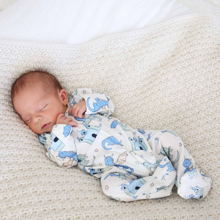 Newborn lounging in zip-up dragon pajamas on a textured knit blanket