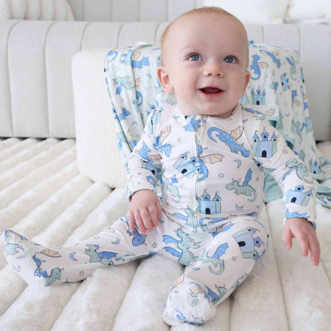 Smiling baby in cream-colored romper with blue and green dragons