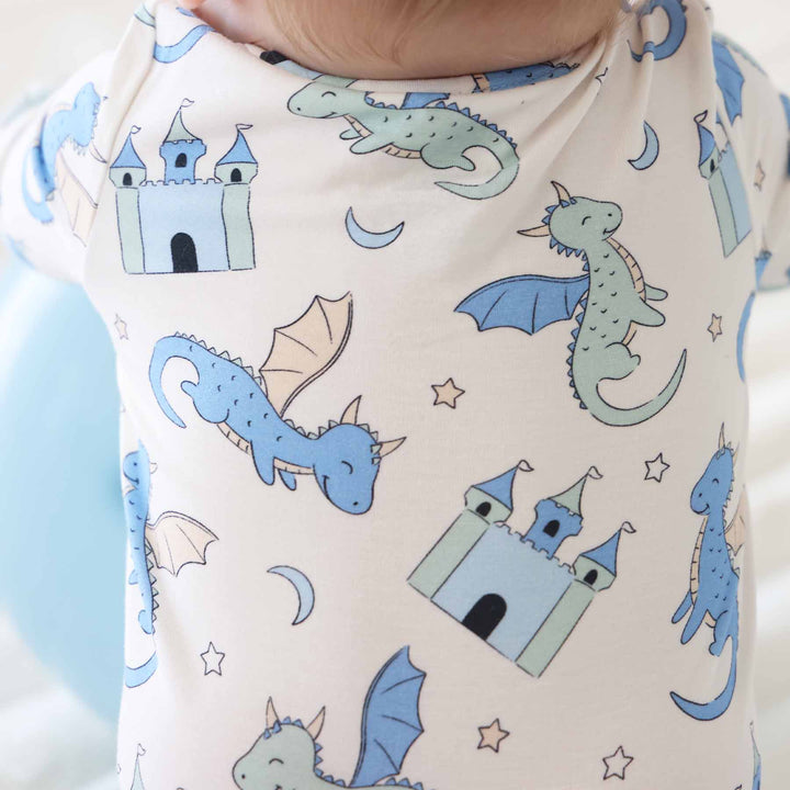Infant outfit featuring blue and green dragon illustrations on a cream background