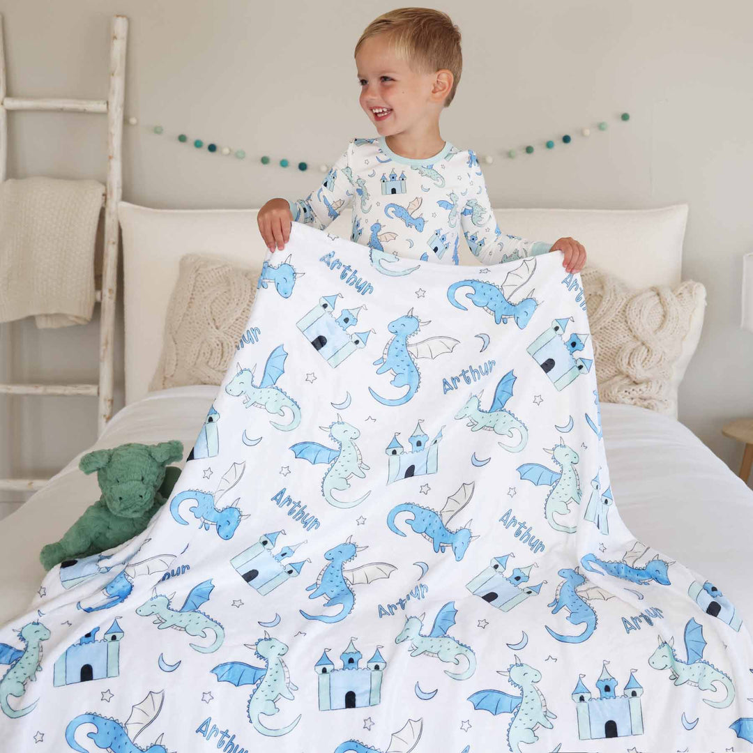 boy holding personalized kids blanket with dragons and castles wearing a matching pajama set 