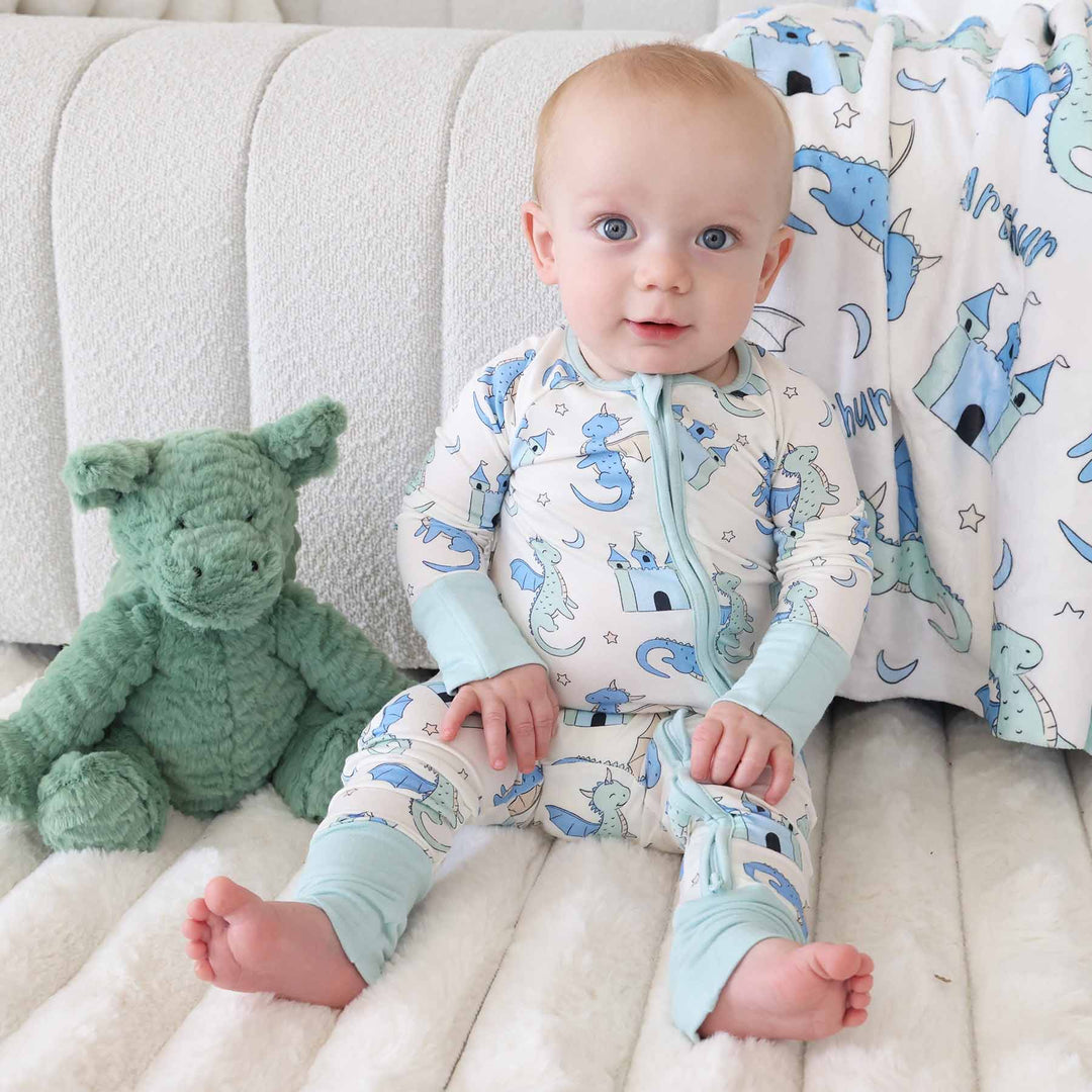 Baby sitting barefoot wearing dragon romper with zipper front