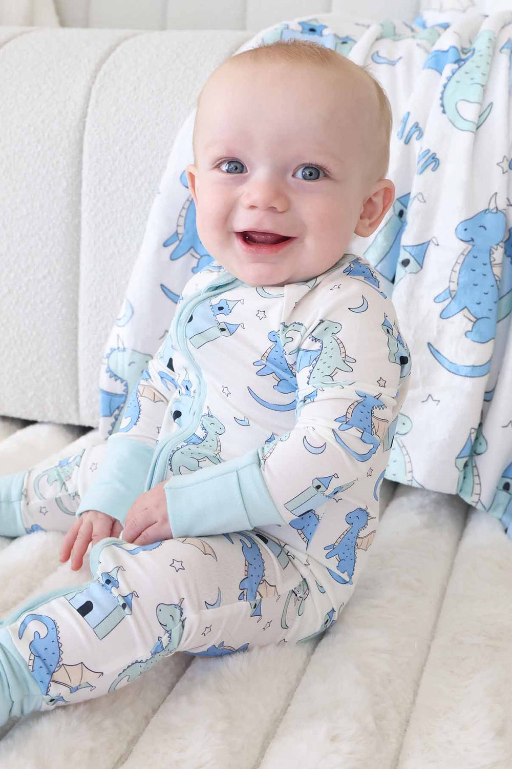 Baby in castle and dragon print romper sitting next to plush toy